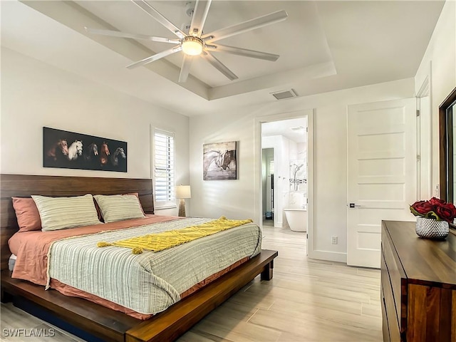 bedroom with light hardwood / wood-style floors, ensuite bathroom, ceiling fan, and a tray ceiling