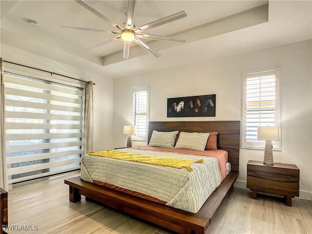 bedroom with light wood-type flooring, a raised ceiling, ceiling fan, and multiple windows