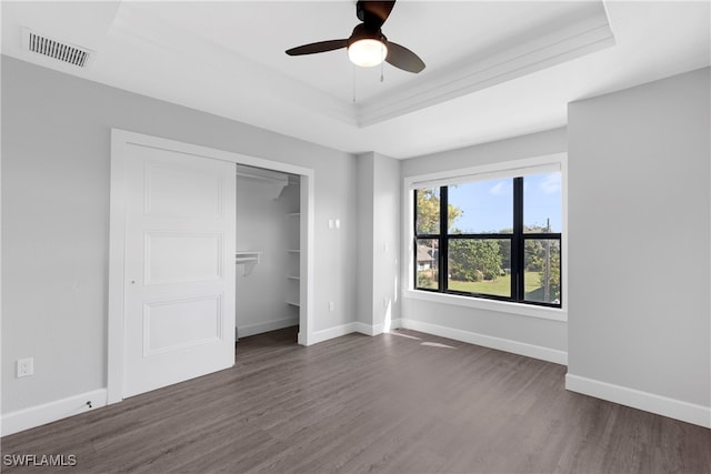 unfurnished bedroom with dark hardwood / wood-style floors, ceiling fan, a closet, and a raised ceiling