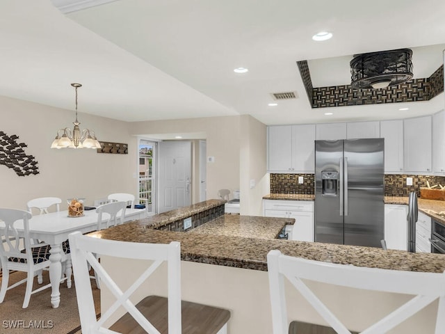 kitchen featuring a kitchen bar, white cabinetry, dark stone countertops, pendant lighting, and stainless steel fridge