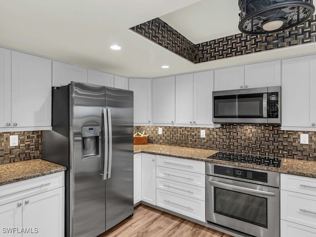 kitchen featuring light wood-type flooring, white cabinets, stainless steel appliances, and dark stone countertops