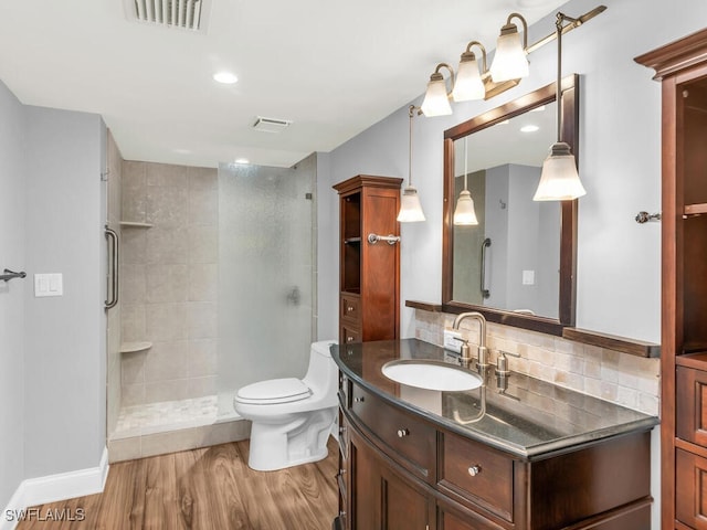 bathroom featuring toilet, hardwood / wood-style flooring, walk in shower, decorative backsplash, and vanity