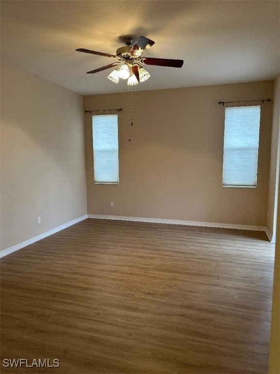 empty room featuring ceiling fan, baseboards, dark wood finished floors, and a wealth of natural light