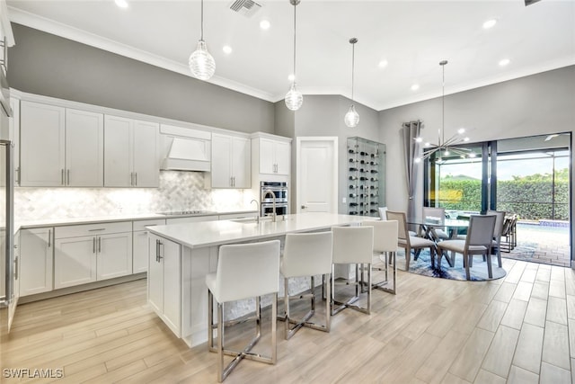 kitchen with pendant lighting, white cabinetry, an island with sink, and premium range hood