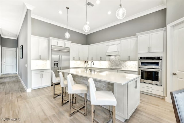 kitchen with sink, custom exhaust hood, hanging light fixtures, appliances with stainless steel finishes, and a kitchen breakfast bar