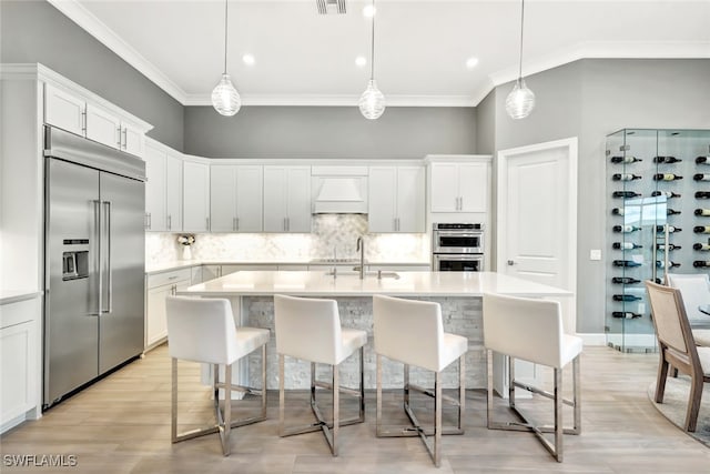 kitchen with decorative light fixtures, stainless steel appliances, white cabinets, and premium range hood