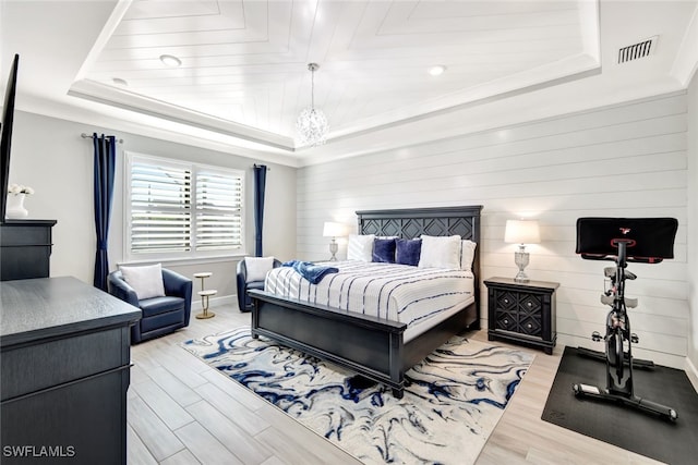 bedroom with a raised ceiling, light wood-type flooring, and a notable chandelier