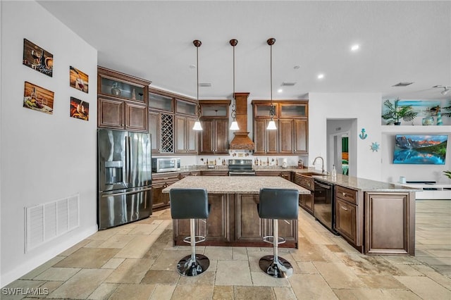 kitchen with premium range hood, kitchen peninsula, appliances with stainless steel finishes, decorative light fixtures, and light stone countertops