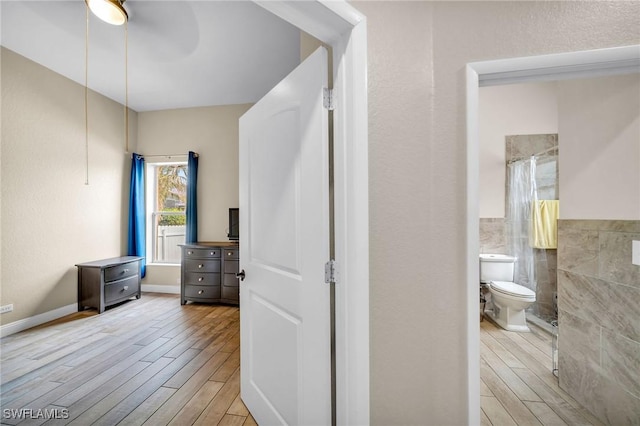 bathroom with toilet, hardwood / wood-style flooring, ceiling fan, tile walls, and walk in shower