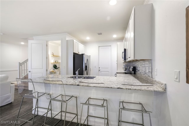 kitchen featuring kitchen peninsula, a kitchen bar, appliances with stainless steel finishes, light stone countertops, and white cabinets