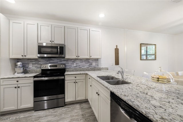 kitchen featuring stainless steel appliances, decorative backsplash, white cabinets, light stone counters, and sink