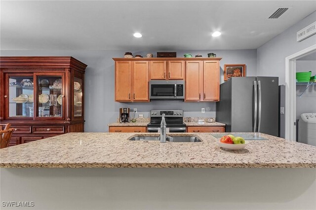 kitchen featuring washer / clothes dryer, light stone countertops, an island with sink, and stainless steel appliances