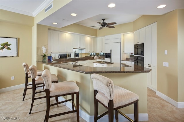 kitchen featuring paneled refrigerator, kitchen peninsula, a kitchen bar, dark stone counters, and white cabinets