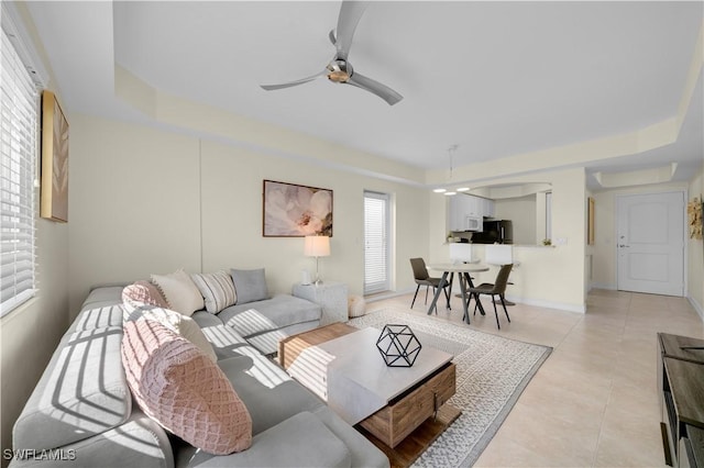 living room with ceiling fan, light tile patterned floors, plenty of natural light, and a tray ceiling