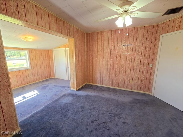 empty room featuring ceiling fan, dark carpet, and wooden walls