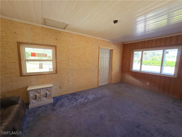 unfurnished living room featuring brick wall, ornamental molding, dark colored carpet, and wooden walls