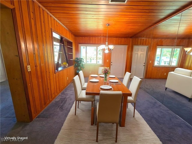 carpeted dining space featuring wood ceiling, a chandelier, and wooden walls