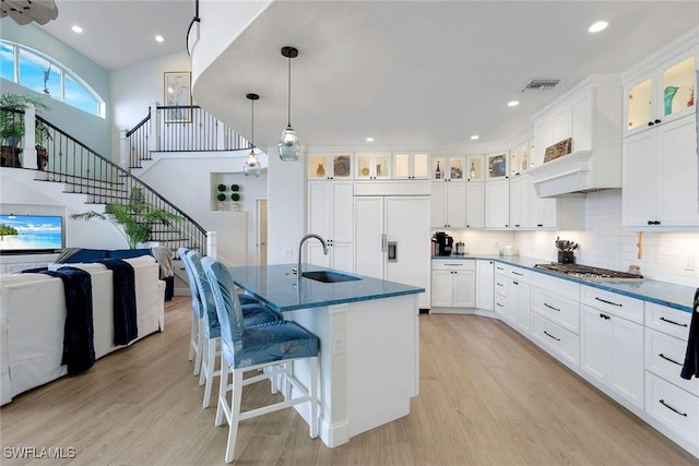 kitchen with dark stone countertops, sink, white cabinetry, paneled fridge, and an island with sink