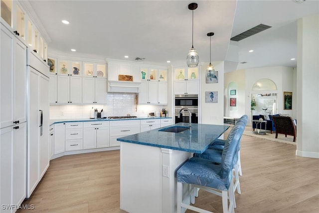 kitchen featuring white cabinets, a kitchen bar, stainless steel appliances, an island with sink, and sink