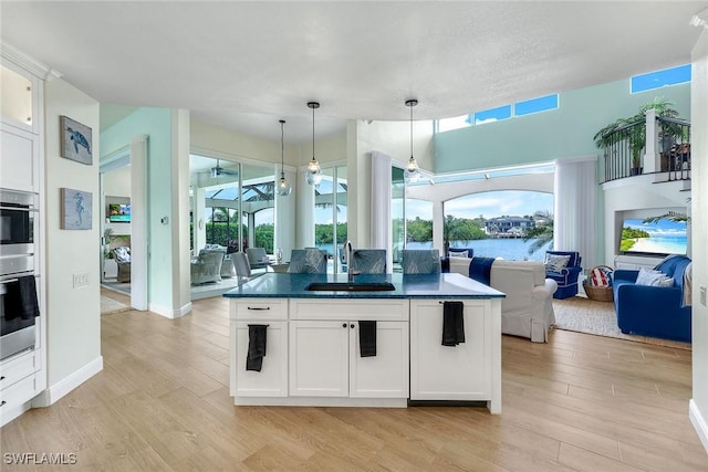 kitchen featuring decorative light fixtures, light hardwood / wood-style floors, sink, a wealth of natural light, and white cabinets