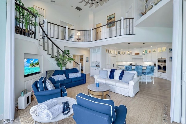 living room with ceiling fan, light hardwood / wood-style flooring, and a towering ceiling