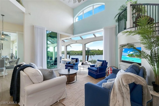 living room featuring ceiling fan, a high ceiling, light hardwood / wood-style flooring, and a water view