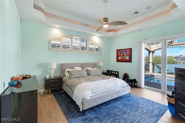 bedroom with a raised ceiling, hardwood / wood-style floors, access to outside, and ceiling fan