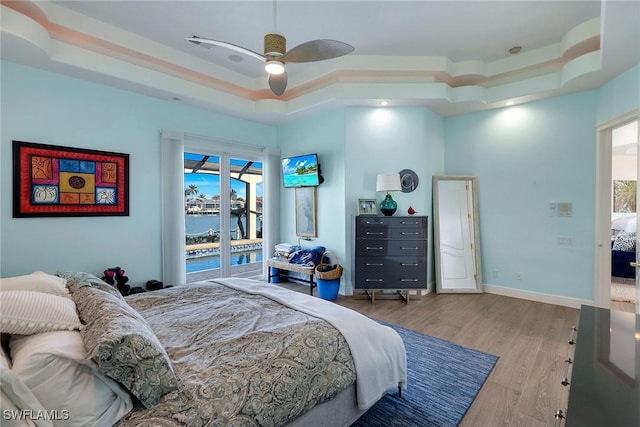 bedroom featuring ceiling fan, access to exterior, a raised ceiling, and light hardwood / wood-style floors