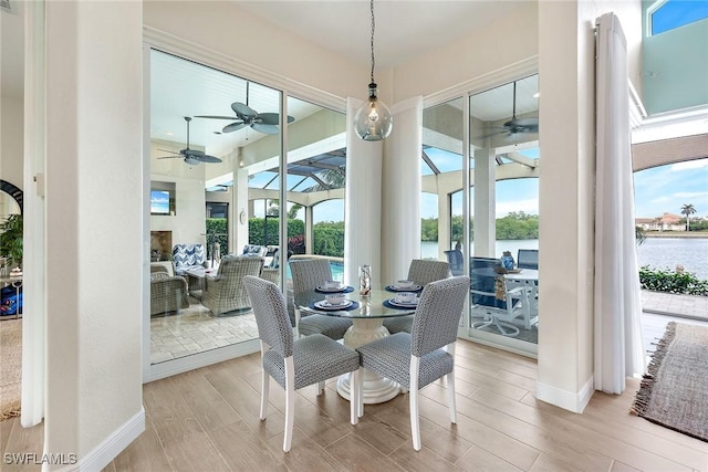 dining room featuring a healthy amount of sunlight, a water view, ceiling fan, and wood finished floors