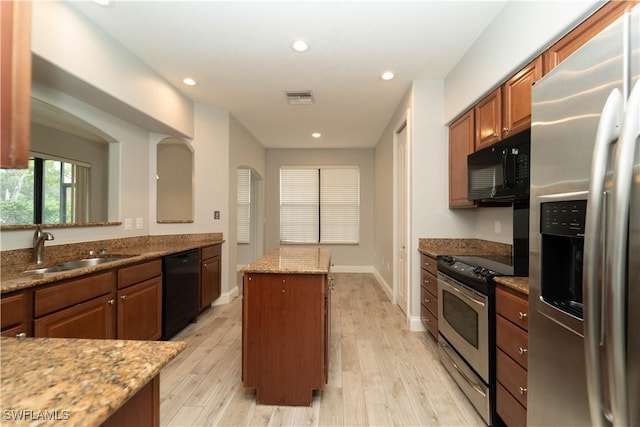 kitchen with light stone counters, light hardwood / wood-style flooring, a center island, black appliances, and sink