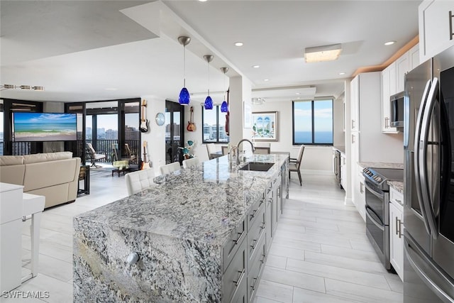 kitchen featuring sink, a large island with sink, appliances with stainless steel finishes, light stone countertops, and white cabinets