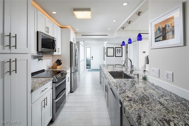 kitchen with sink, appliances with stainless steel finishes, white cabinetry, light stone counters, and decorative light fixtures