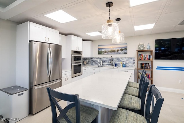 kitchen featuring sink, white cabinetry, stainless steel appliances, decorative backsplash, and decorative light fixtures