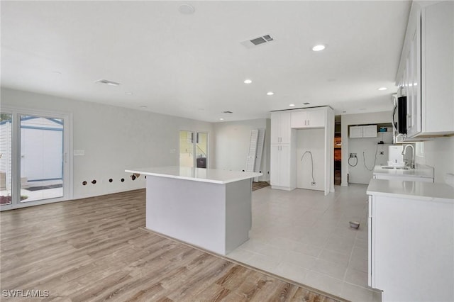 kitchen with white cabinets, a kitchen island, light wood-type flooring, and sink