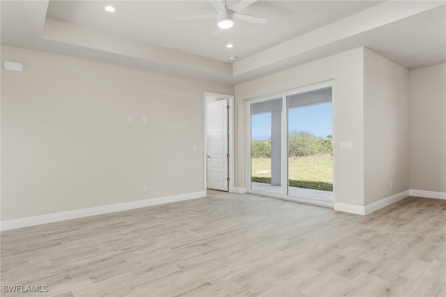 empty room with ceiling fan, a tray ceiling, and light hardwood / wood-style floors