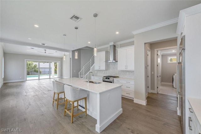 kitchen with appliances with stainless steel finishes, white cabinetry, sink, an island with sink, and wall chimney exhaust hood