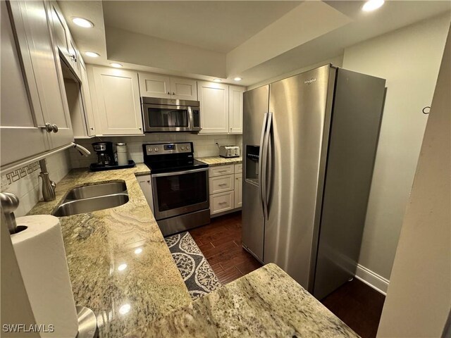 kitchen featuring light stone countertops, appliances with stainless steel finishes, decorative backsplash, sink, and dark hardwood / wood-style floors