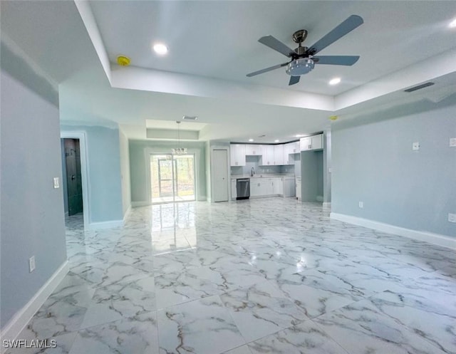 unfurnished living room with ceiling fan with notable chandelier, sink, and a tray ceiling