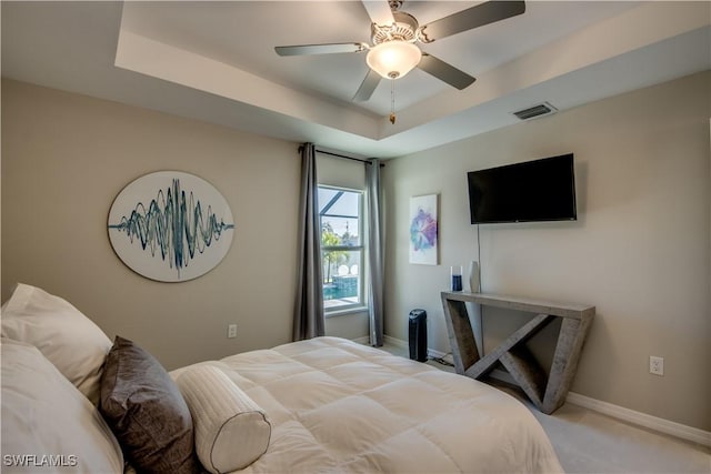 carpeted bedroom with ceiling fan and a raised ceiling