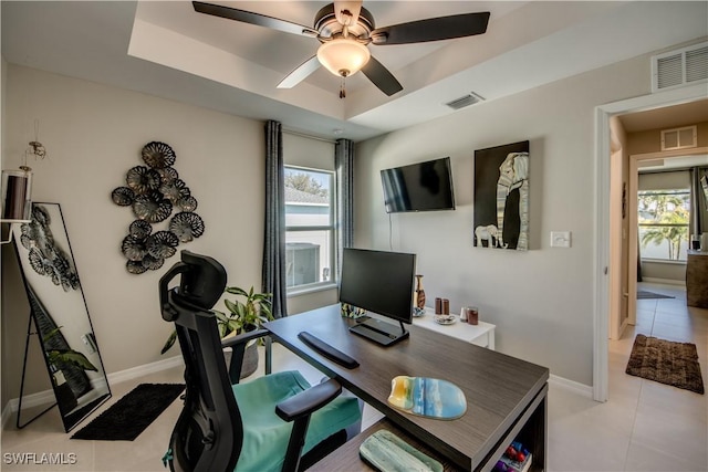 office space with ceiling fan, plenty of natural light, light tile patterned floors, and a raised ceiling