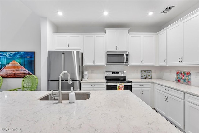 kitchen with appliances with stainless steel finishes, white cabinetry, decorative backsplash, sink, and light stone counters