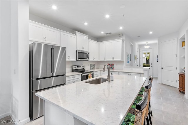 kitchen with white cabinets, an island with sink, light stone counters, and stainless steel appliances