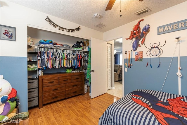 bedroom with a textured ceiling, ceiling fan, light wood-type flooring, and a closet