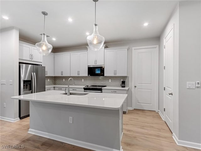 kitchen featuring decorative light fixtures, white cabinets, appliances with stainless steel finishes, and an island with sink