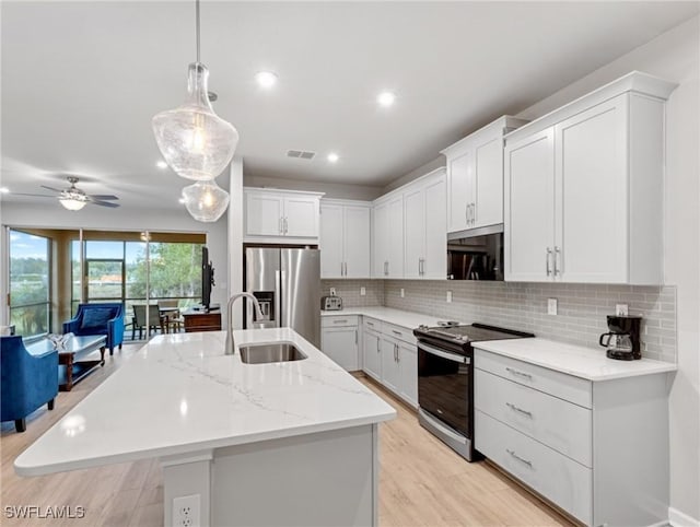 kitchen with white cabinetry, hanging light fixtures, stainless steel appliances, and an island with sink