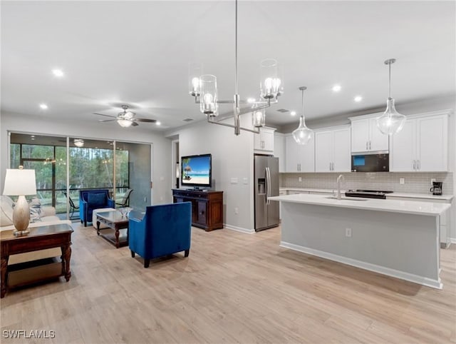 kitchen with hanging light fixtures, appliances with stainless steel finishes, backsplash, white cabinetry, and a kitchen island with sink