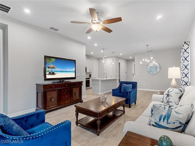 living room with sink, light hardwood / wood-style floors, and ceiling fan with notable chandelier