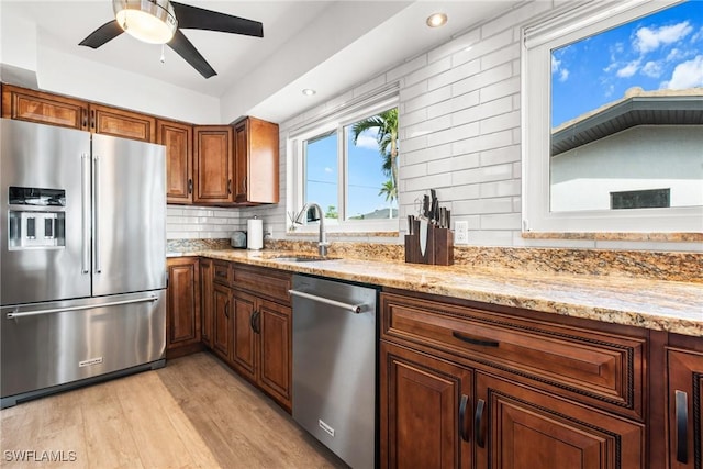 kitchen with light hardwood / wood-style floors, stainless steel appliances, tasteful backsplash, light stone counters, and sink