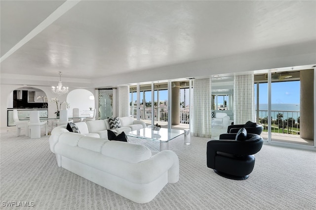 living room with an inviting chandelier, light carpet, a wealth of natural light, and a water view