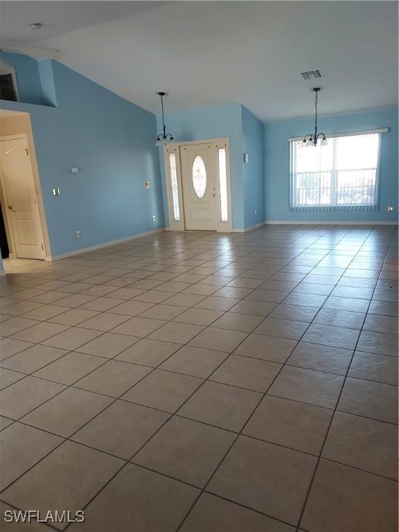 unfurnished living room featuring an inviting chandelier, light tile patterned floors, and high vaulted ceiling